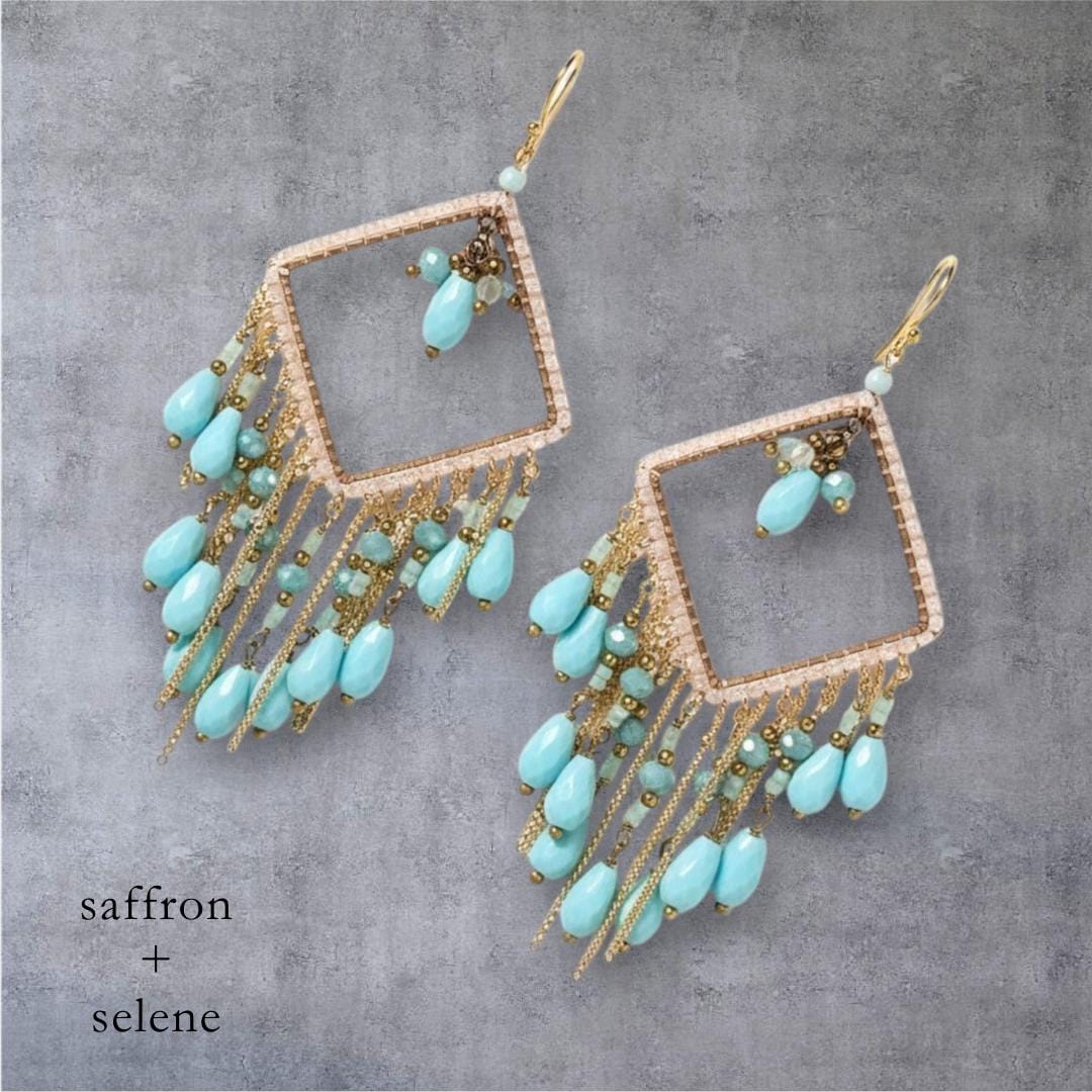 A pair of gold-toned, square-shaped earrings with turquoise teardrop beads and delicate gold chains. The earrings feature a fringe of turquoise beads and smaller gold beads, with the text "saffron + selene" at the bottom.