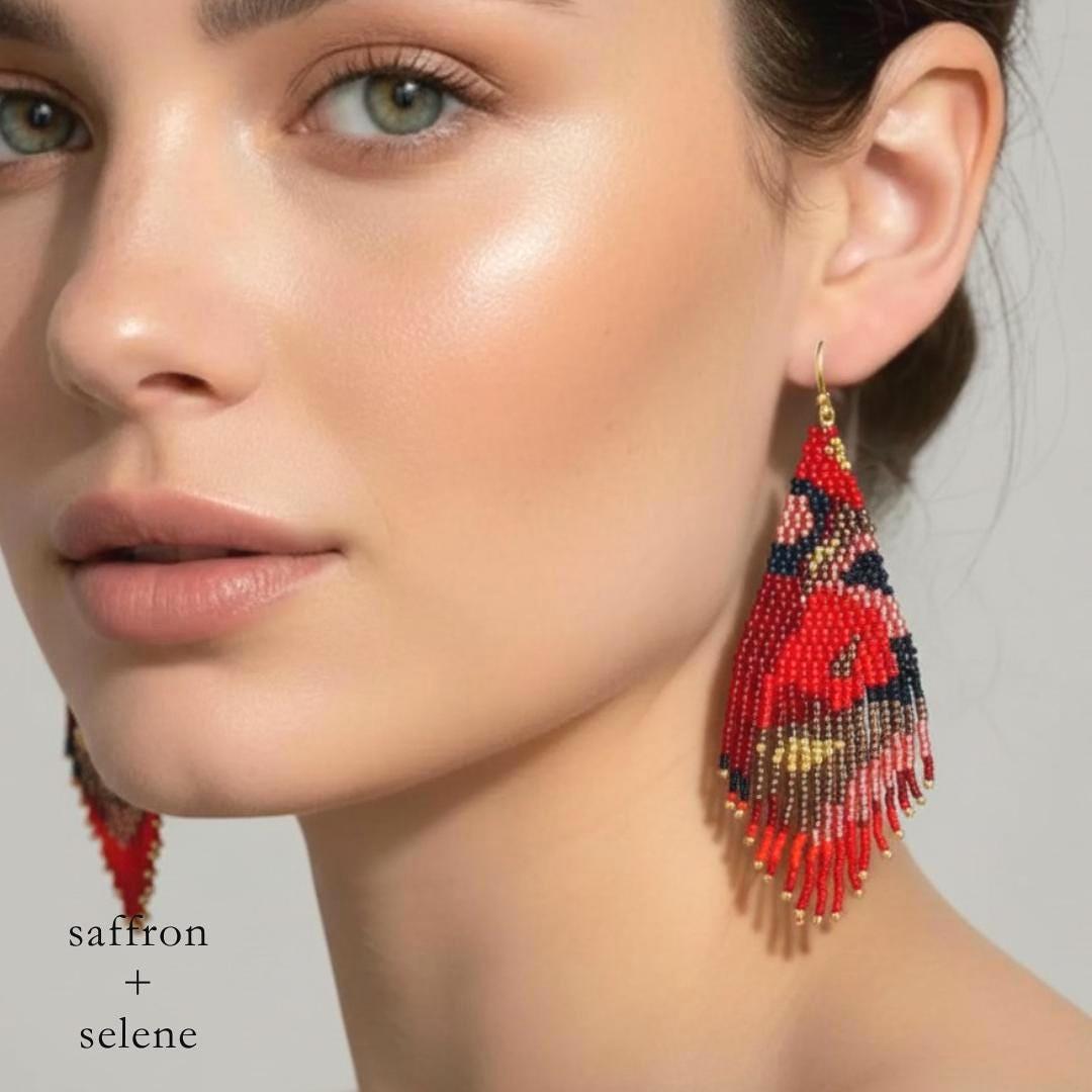 Model wears Red, black, and gold fringe  beaded earrings.  Handmade statement earrings with an abstract floral design, created by Saffron and Selene Boho Jewelry