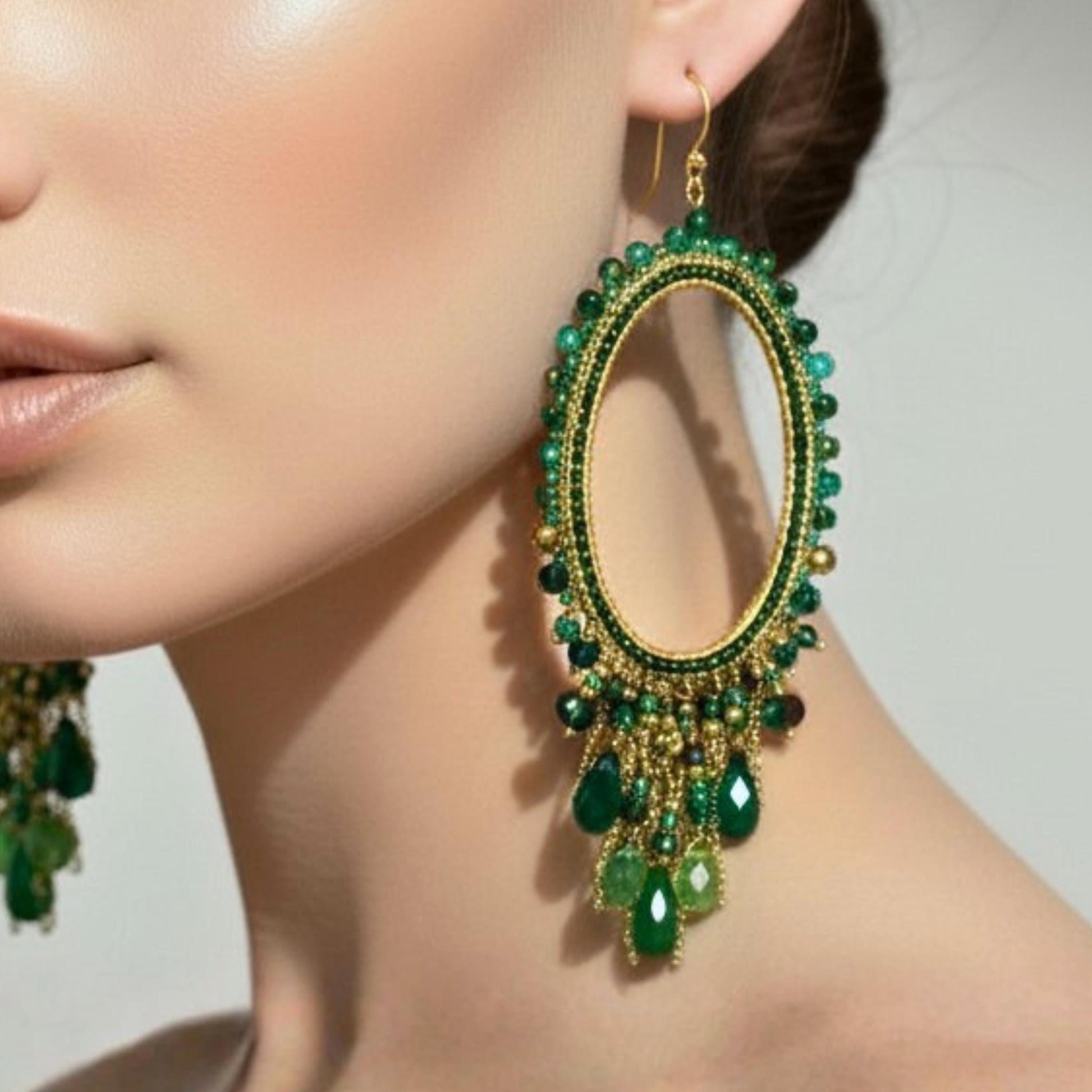 Close up of womens boho statement green beaded dangling earrings.  Four inch drop suspended off an oval brushed gold frame.  By Saffron and Selene