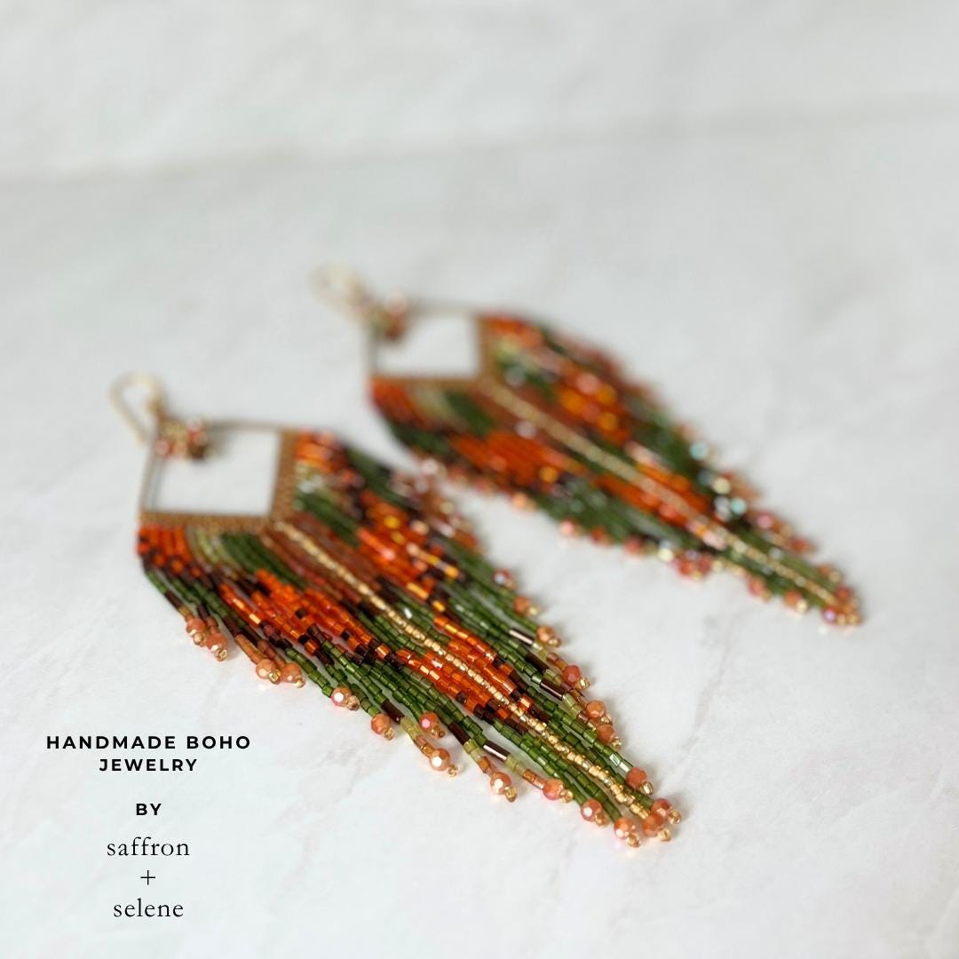 Long orange and green fringe earrings featuring a gold geometric frame and flowing artisan beadwork.